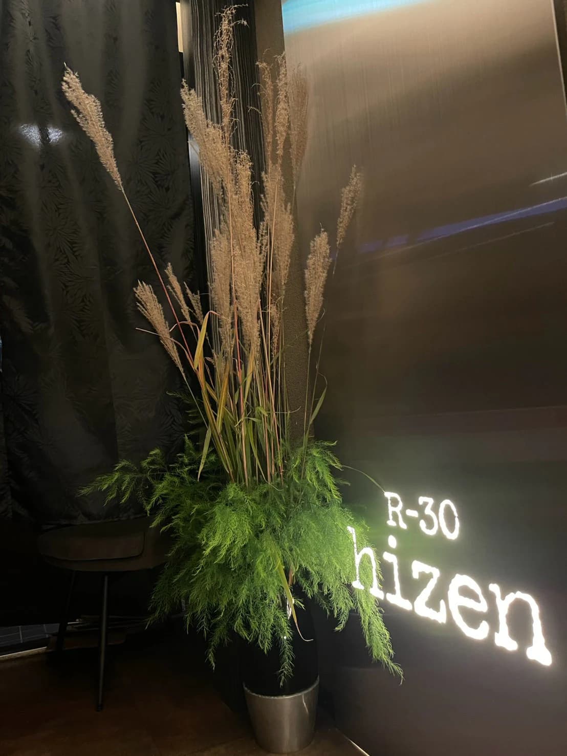 R-30 hizenの入口。壁に浮かぶロゴと、すすきの穂を生けた花器